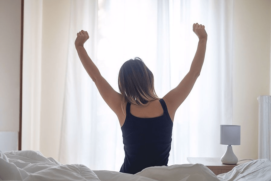 Frau sitzt auf Bett und streckt sich